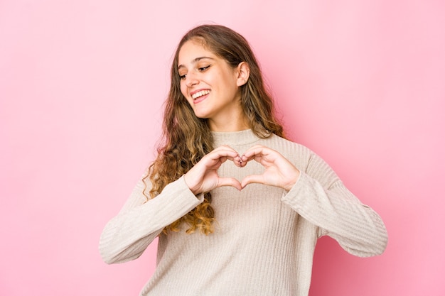 Jonge kaukasische vrouw die en een hartvorm met handen glimlacht toont.