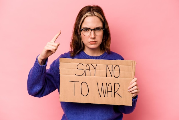 Jonge kaukasische vrouw die geen oorlogsaanplakbiljet houdt dat op roze achtergrond wordt geïsoleerd