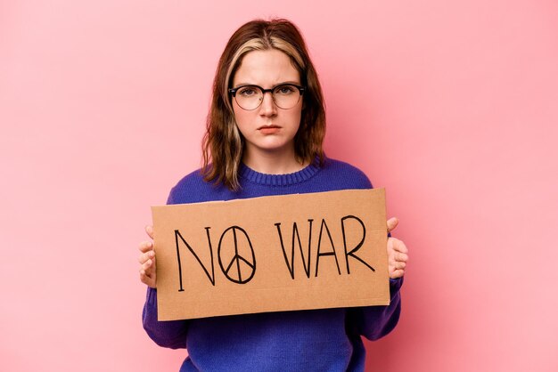 Jonge kaukasische vrouw die geen oorlogsaanplakbiljet houdt dat op roze achtergrond wordt geïsoleerd