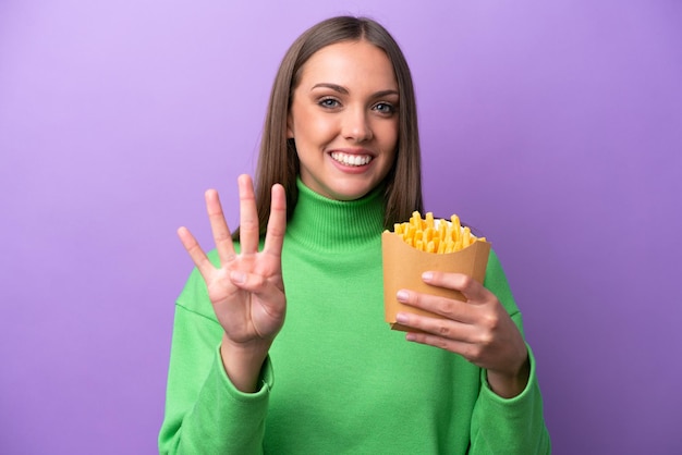 Jonge kaukasische vrouw die gefrituurde chips op een paarse achtergrond houdt, gelukkig en vier met vingers telt