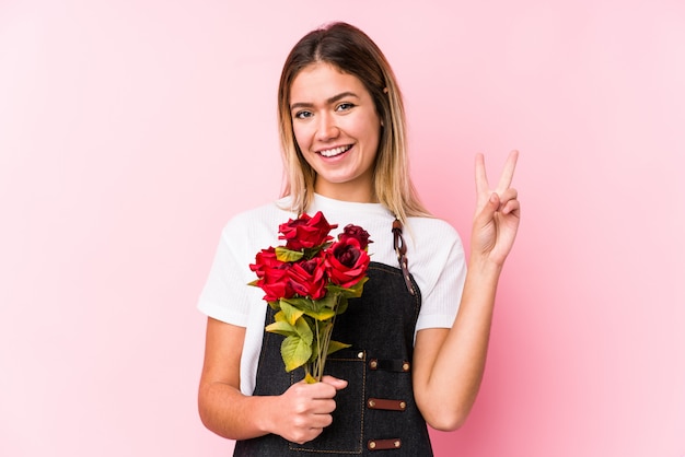 Jonge Kaukasische vrouw die geïsoleerde rozen houden tonend nummer twee met vingers.