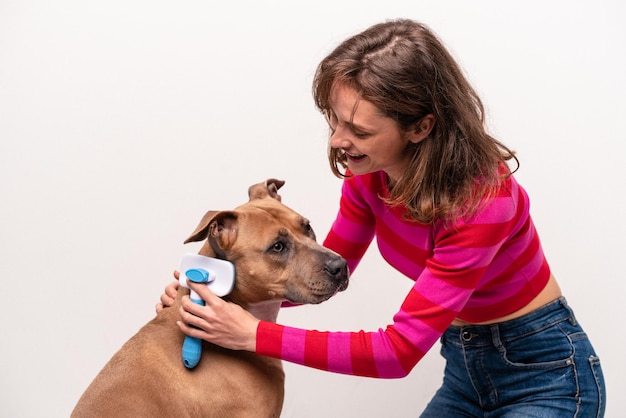 Jonge kaukasische vrouw die haar hond kamt die op witte achtergrond wordt geïsoleerd