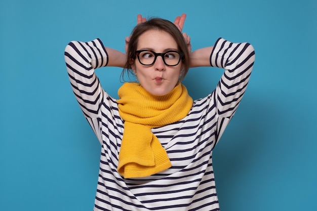 Foto jonge kaukasische vrouw die in glazen vissengezicht maakt. studio opname op blauwe muur.