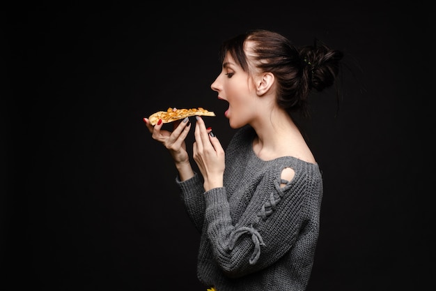 Jonge kaukasische vrouw die met staart stuk van pizza eet.