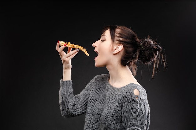 Jonge Kaukasische vrouw die met staart stuk van pizza eet.