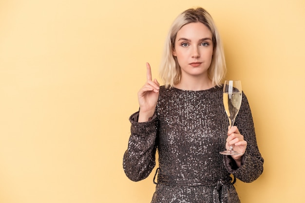 Jonge kaukasische vrouw die Nieuwjaar viert dat op gele achtergrond wordt geïsoleerd die nummer één met vinger toont.