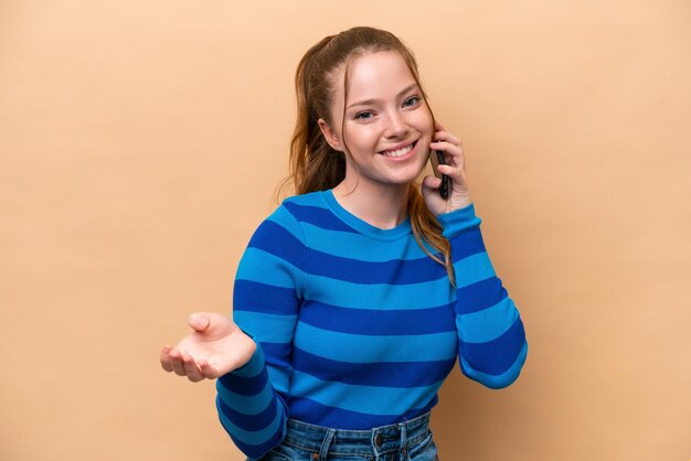 Jonge kaukasische vrouw die op beige achtergrond een gesprek met de mobiele telefoon met iemand houdt