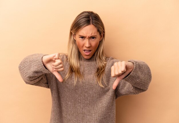 Foto jonge kaukasische vrouw die op beige achtergrond wordt geïsoleerd die duim omlaag toont en afkeer uitdrukt.