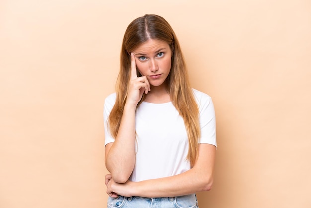 Jonge kaukasische vrouw die op beige achtergrond wordt geïsoleerd die een idee denkt