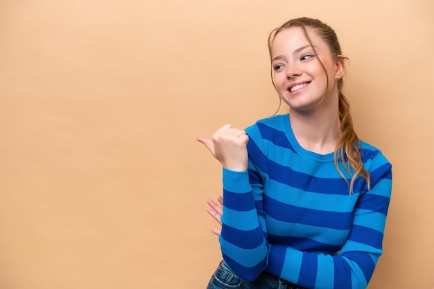 Jonge kaukasische vrouw die op beige achtergrond wordt geïsoleerd die naar de kant wijst om een product te presenteren