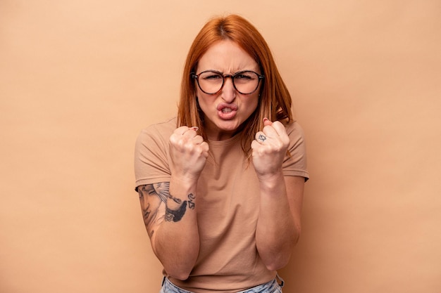 Foto jonge kaukasische vrouw die op beige achtergrond wordt geïsoleerd die vuist toont aan camera agressieve gezichtsuitdrukking