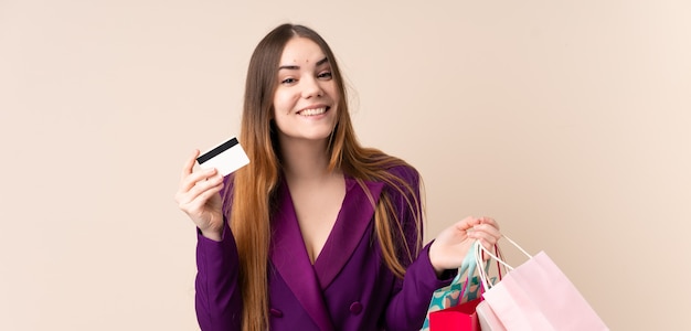 Jonge Kaukasische vrouw die op beige het winkelen van de muurholding zakken en een creditcard wordt geïsoleerd