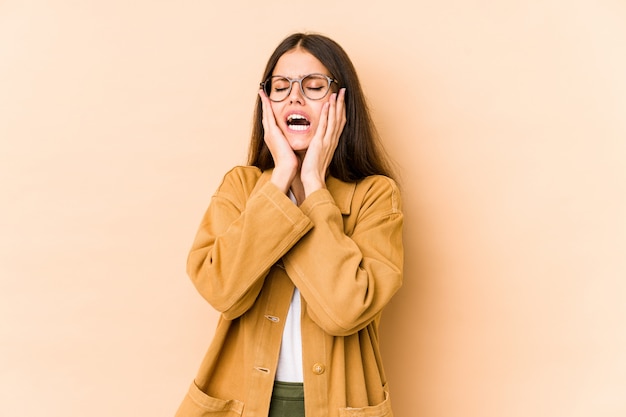 Jonge Kaukasische vrouw die op beige muur wordt geïsoleerd die troosteloos zeurt.