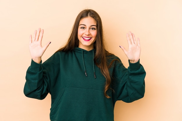 Jonge Kaukasische vrouw die op beige wordt geïsoleerd dat aantal ton met handen toont.