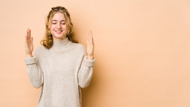 Jonge Kaukasische vrouw die op beige wordt geïsoleerd die blij lacht. Geluk concept.