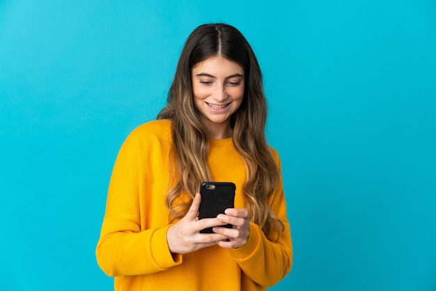 Jonge kaukasische vrouw die op blauw een bericht of e-mail met mobiel verzendt