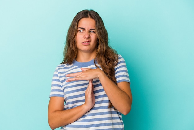 Jonge kaukasische vrouw die op blauwe achtergrond wordt geïsoleerd die een time-outgebaar toont.