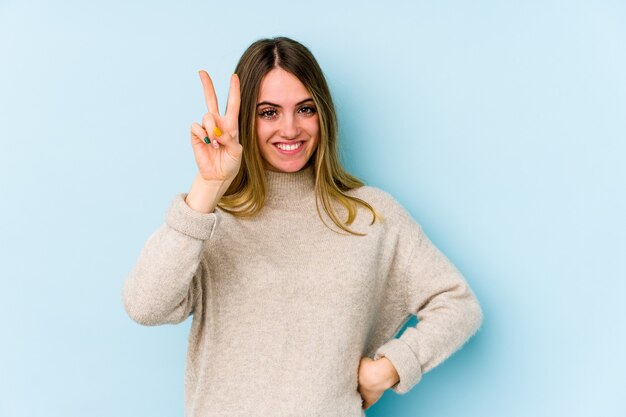 Jonge kaukasische vrouw die op blauwe achtergrond wordt geïsoleerd die nummer twee met vingers toont.