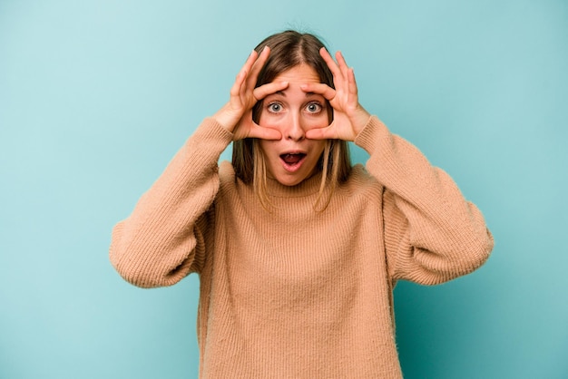 Jonge kaukasische vrouw die op blauwe achtergrond wordt geïsoleerd die ogen open houdt om een succeskans te vinden