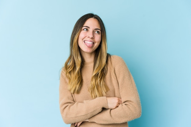 Jonge kaukasische vrouw die op blauwe muur grappige en vriendschappelijke tong uitsteekt.