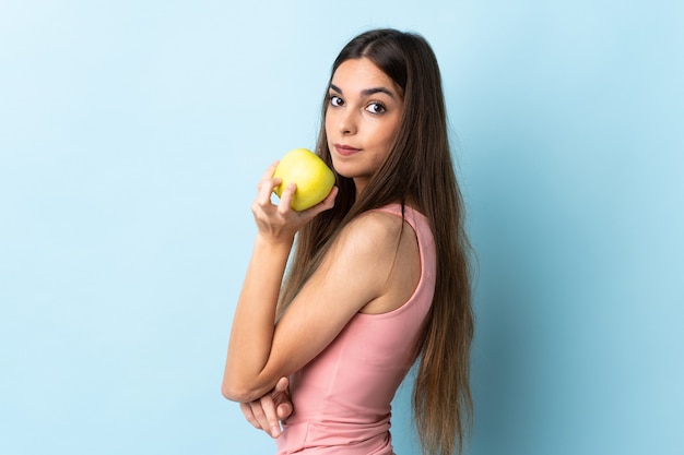 Jonge kaukasische vrouw die op blauwe muur wordt geïsoleerd die een appel eet