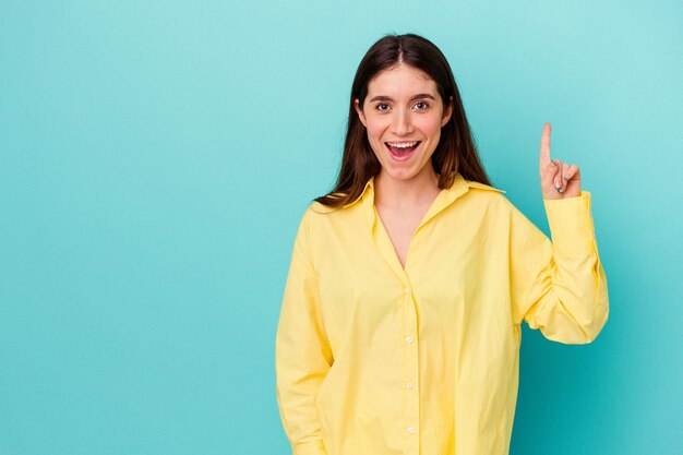 Jonge kaukasische vrouw die op blauwe muur wordt geïsoleerd die nummer één met vinger toont.