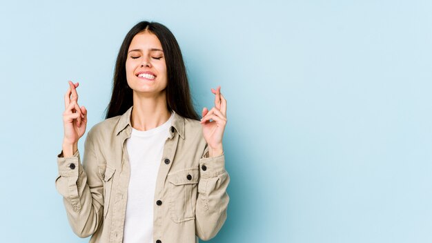 Jonge Kaukasische vrouw die op blauwe muur wordt geïsoleerd die vingers kruist voor het hebben van geluk