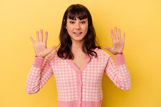 Jonge kaukasische vrouw die op gele achtergrond wordt geïsoleerd die nummer tien met handen toont.