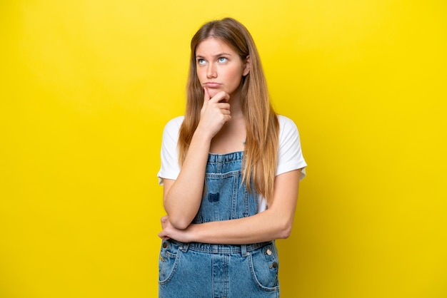 Jonge kaukasische vrouw die op gele achtergrond wordt geïsoleerd die twijfels heeft