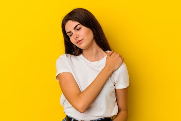 Jonge kaukasische vrouw die op gele muur wordt geïsoleerd die een schouderpijn heeft.