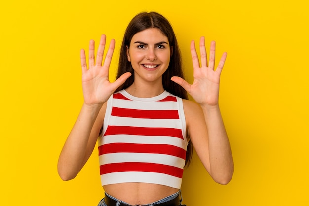 Jonge kaukasische vrouw die op gele muur wordt geïsoleerd die nummer tien met handen toont.