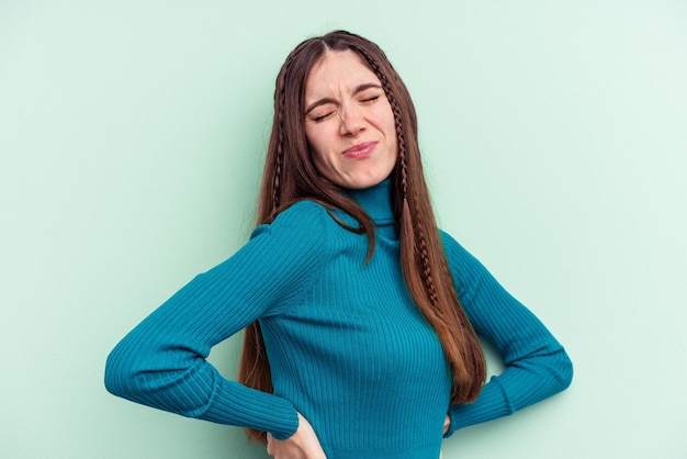 Jonge kaukasische vrouw die op groene achtergrond wordt geïsoleerd die aan rugpijn lijdt.