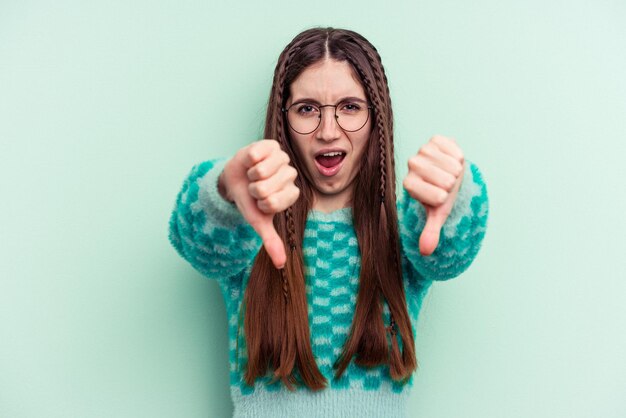 Jonge kaukasische vrouw die op groene achtergrond wordt geïsoleerd die duim omlaag toont en afkeer uitdrukt.