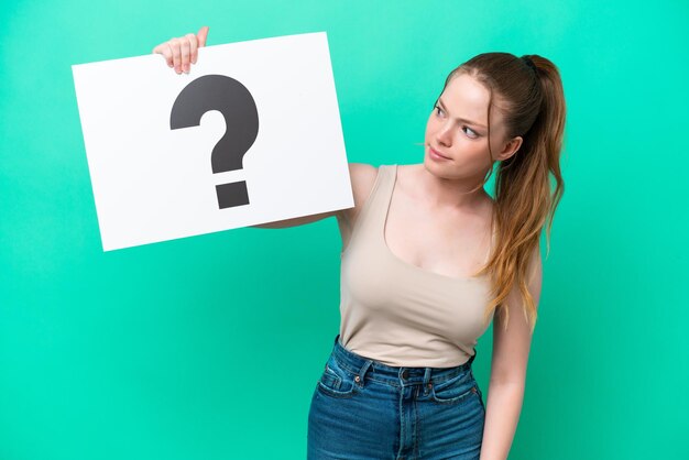 Jonge kaukasische vrouw die op groene achtergrond wordt geïsoleerd die een plakkaat met vraagtekensymbool houdt