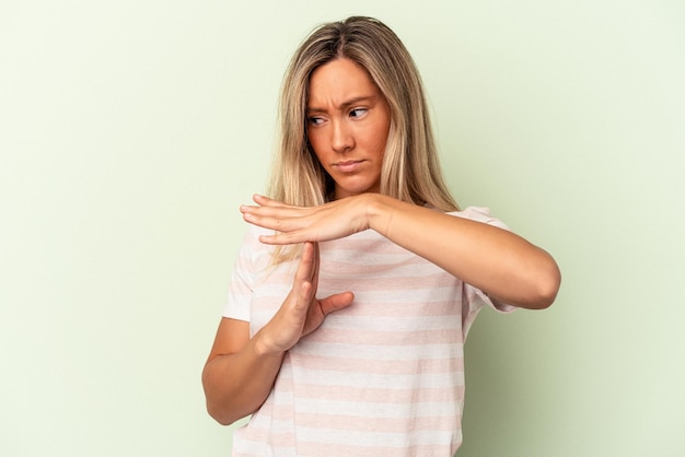 Jonge kaukasische vrouw die op groene achtergrond wordt geïsoleerd die een time-outgebaar toont.