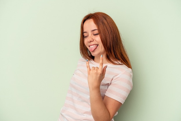 Jonge kaukasische vrouw die op groene achtergrond wordt geïsoleerd die rotsgebaar met vingers toont