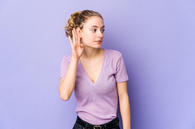 Jonge kaukasische vrouw die op purpere ruimte probeert een roddel te luisteren.