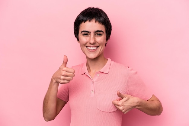 Jonge kaukasische vrouw die op roze achtergrond wordt geïsoleerd die beide duimen opheft glimlachend en zelfverzekerd?