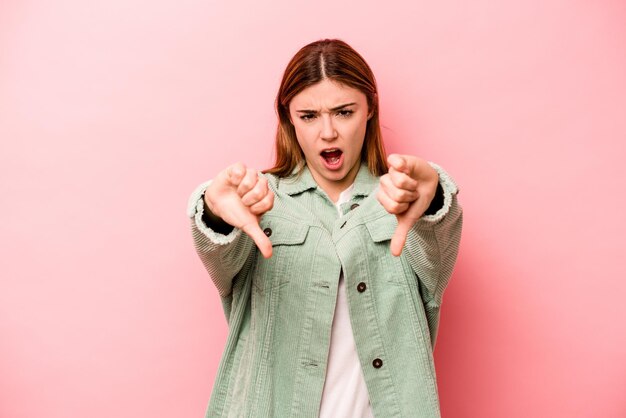 Jonge kaukasische vrouw die op roze achtergrond wordt geïsoleerd die duim omlaag toont en afkeer uitdrukt