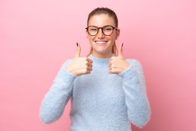 Jonge kaukasische vrouw die op roze achtergrond wordt geïsoleerd die een duim omhoog gebaar geeft