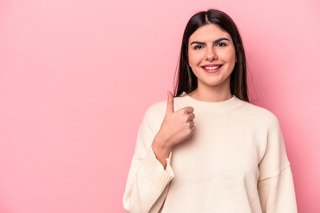 Jonge kaukasische vrouw die op roze achtergrond wordt geïsoleerd die en duim glimlacht opheft