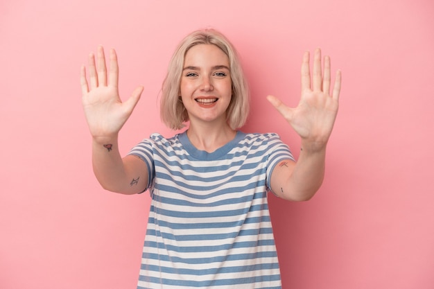 Jonge kaukasische vrouw die op roze achtergrond wordt geïsoleerd die nummer tien met handen toont.