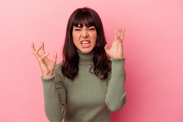 Jonge kaukasische vrouw die op roze achtergrond wordt geïsoleerd die van woede schreeuwt.