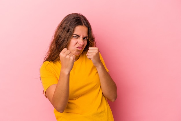 Jonge kaukasische vrouw die op roze achtergrond wordt geïsoleerd die vuist toont aan camera, agressieve gezichtsuitdrukking.