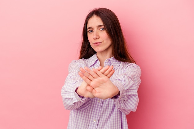 Jonge kaukasische vrouw die op roze achtergrond wordt geïsoleerd die zich met uitgestrekte hand bevindt die stopbord toont, die u verhinderen.