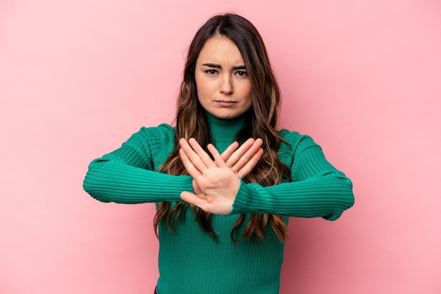 Jonge kaukasische vrouw die op roze achtergrond wordt geïsoleerd die zich met uitgestrekte hand bevindt die stopteken toont dat u verhindert