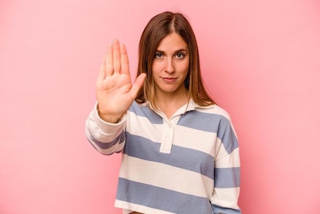 Jonge kaukasische vrouw die op roze achtergrond wordt geïsoleerd die zich met uitgestrekte hand bevindt die stopteken toont dat u verhindert