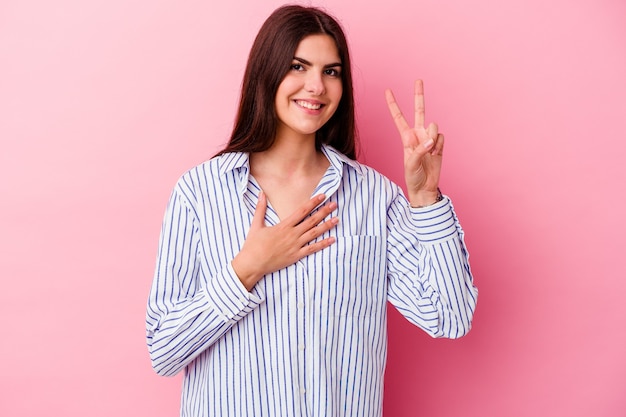 Jonge kaukasische vrouw die op roze een eed aflegt, hand op borst legt.