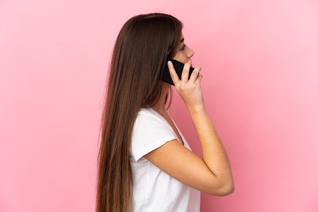 Jonge kaukasische vrouw die op roze muur een gesprek met de mobiele telefoon met iemand houdt