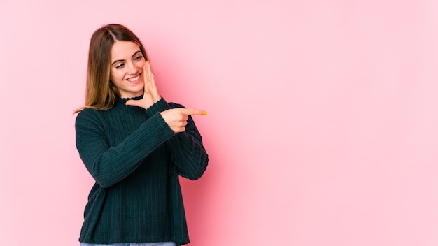 Jonge kaukasische vrouw die op roze muur een roddel zegt